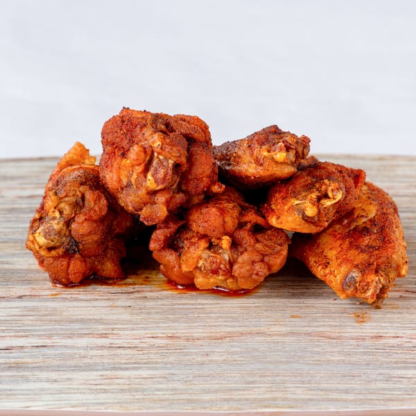 A pile of crispy, seasoned fried chicken pieces from Cluck & Smash on a wooden surface.