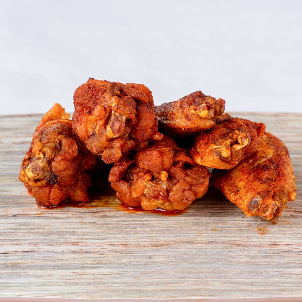 A pile of crispy, seasoned fried chicken pieces from Cluck & Smash on a wooden surface.
