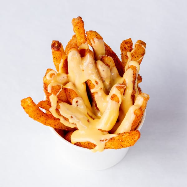 Cluck & Smash seasoned fries, generously topped with melted cheese sauce, served in a white cup.