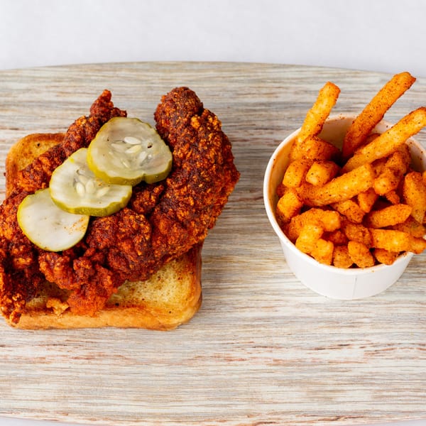 Cluck & Smash fried chicken sandwich with pickles on toast, next to a cup of seasoned fries.