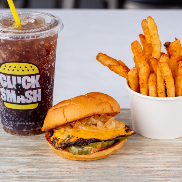 Cluck & Smash cheeseburger with pickles and onions, seasoned fries, and a soda with a yellow straw.